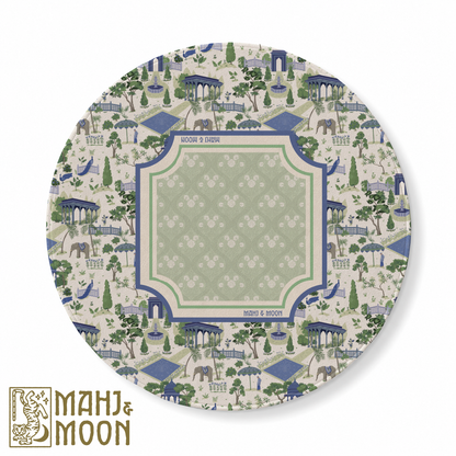 Round American Mahjong mat featuring a blue and sage green garden toile design with pavilions, peacocks, elephants, fountains and botanical motifs surrounding a soft green central playing area.