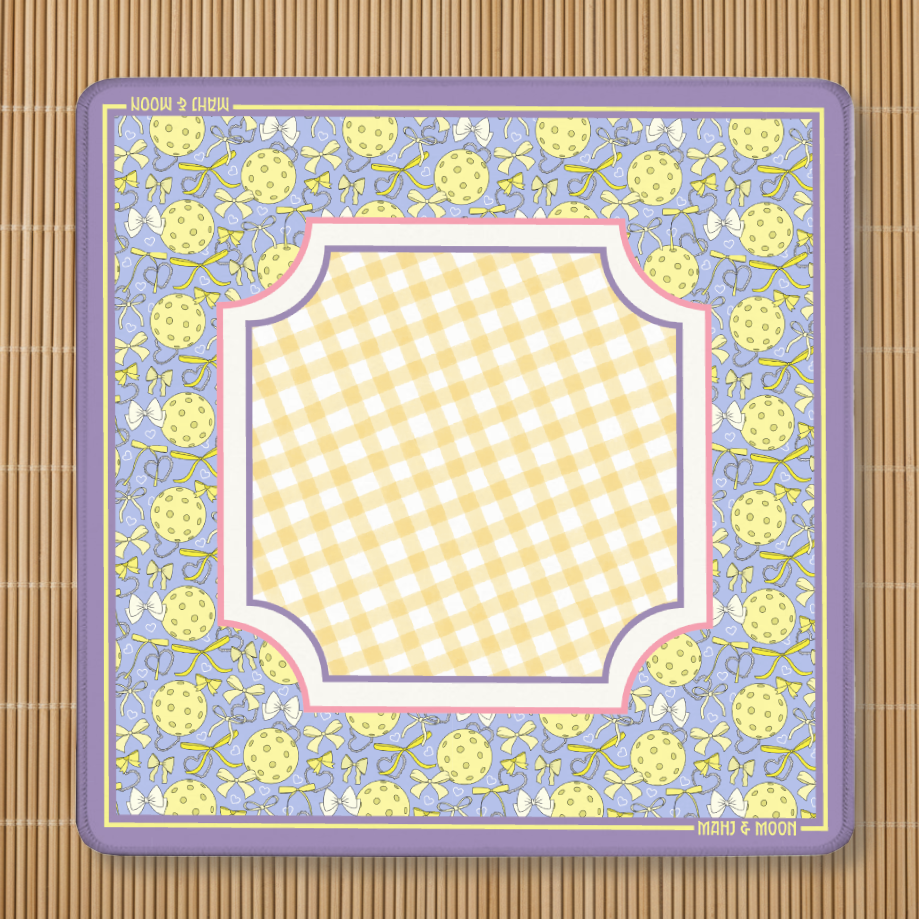 Preppy pickleball-themed American Mahjong mat with a lavender border featuring pickleballs, bows and ribbons surrounding a soft yellow gingham playing centre. Non-slip polyester and rubber Mahjong playing mat by Mahj & Moon.