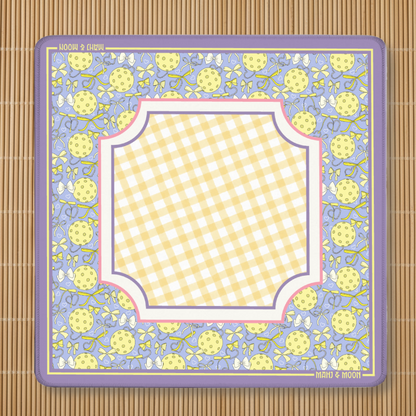 Preppy pickleball-themed American Mahjong mat with a lavender border featuring pickleballs, bows and ribbons surrounding a soft yellow gingham playing centre. Non-slip polyester and rubber Mahjong playing mat by Mahj & Moon.