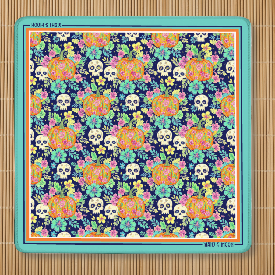 Halloween American Mahjong mat featuring colourful floral pumpkins, sugar skulls and botanical flowers on a navy background with a turquoise border and non-slip rubber backing.
