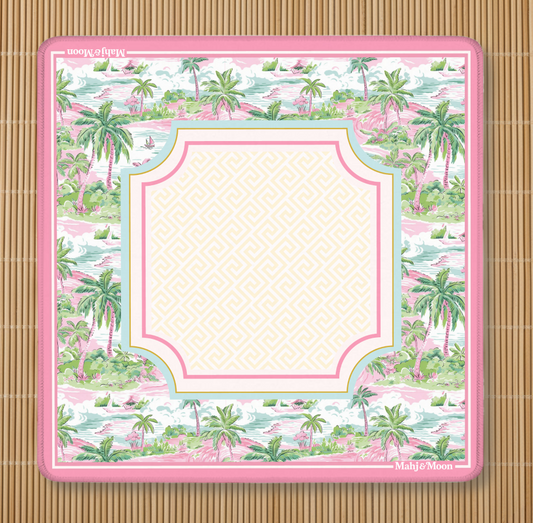 A mahjong mat with palm tree pattern with bright pink border and a light, framed center on a bamboo background